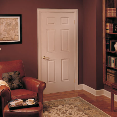A cozy study with a brown leather chair, a cup of tea, and a book. A white six-panel door, a book-filled shelf, and a vintage map on a warm-toned wall.