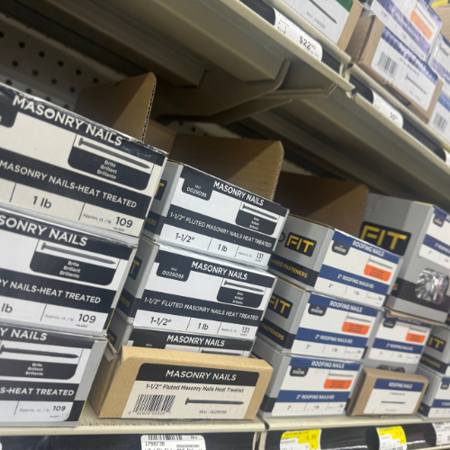 Boxes of masonry nails on store shelves, neatly organized in rows. Product labels and weights are visible, conveying a hardware store setting.