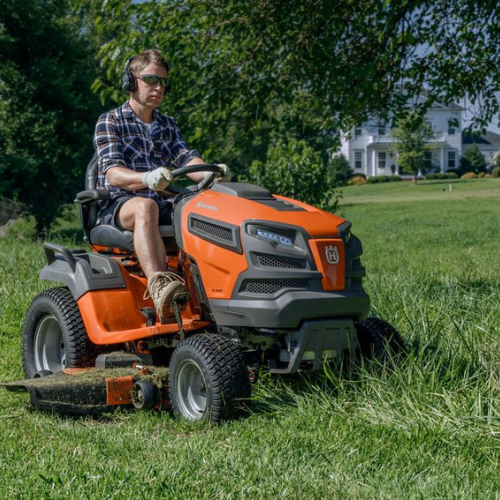 A person on an orange ride-on lawn mower trims grass in a sunny yard. Wearing sunglasses and ear protection, they convey focus and determination.