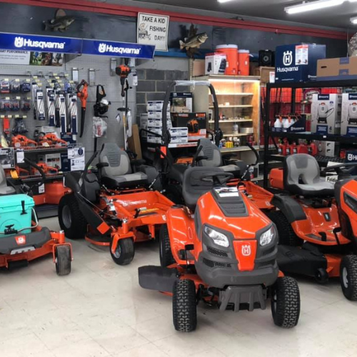 A showroom displaying orange Husqvarna lawnmowers and equipment. The space is organized, with tools on a pegboard and shelves filled with various products.
