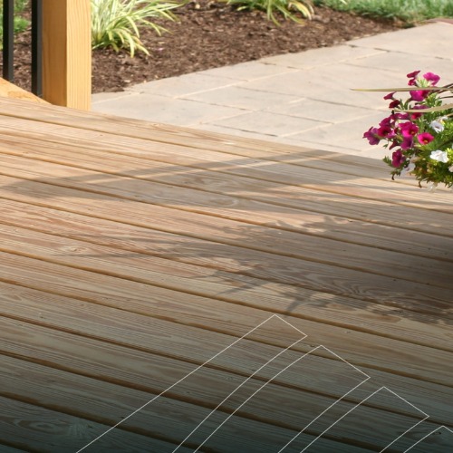 A sunlit wooden deck leads to a stone pathway, bordered by soil. Pink and white flowers in a pot add a touch of color, evoking a serene outdoor vibe.