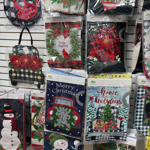 A display of festive garden flags featuring Christmas designs, including snowmen, red trucks, and poinsettias, conveying a cheerful holiday spirit.