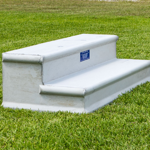Concrete steps on lush green grass. The steps are simple, white, and rectangular, with a blue sign on the riser, creating a clean, functional look.