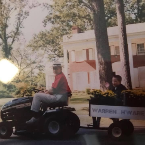 Man on a tractor pulls a child in a small wagon with yellow flowers and 