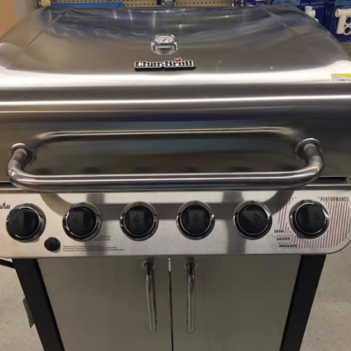 A stainless steel Char-Broil gas grill with a closed lid, featuring five black control knobs and sturdy handles, set in a store display.