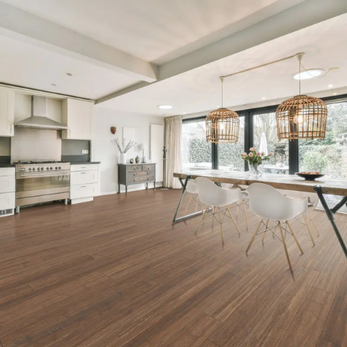 Spacious modern kitchen with wooden floors, featuring a large dining table, wicker pendant lights, white chairs, and stainless steel appliances.