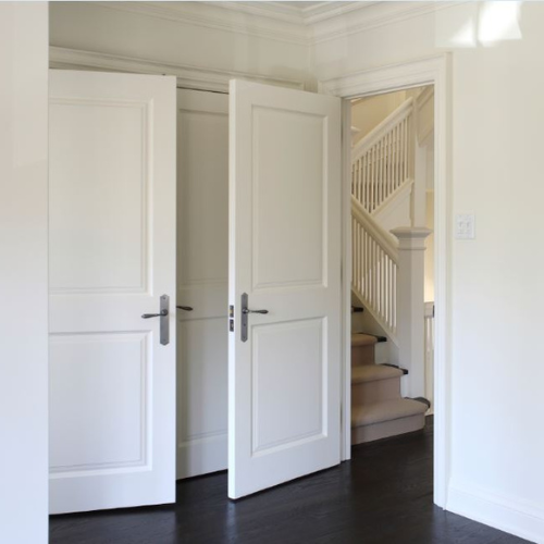 Two white interior doors are partially open, revealing a staircase with white railings. The dark hardwood floor contrasts with the light walls, creating a calm atmosphere.