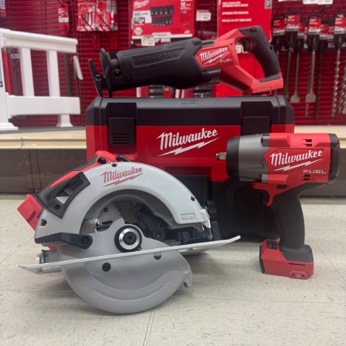 A display of Milwaukee power tools on the floor, including a circular saw, impact wrench, and reciprocating saw, all placed in front of a branded toolbox.
