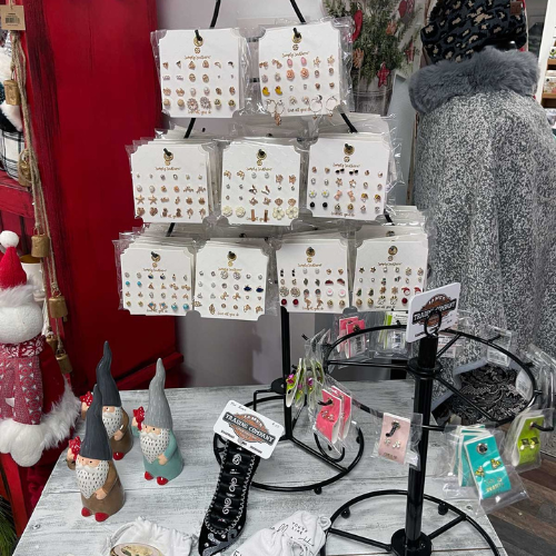 Display of festive earring sets and accessories in a shop. Includes gnome figurines, Santa decor, and various packaged items, creating a cozy holiday vibe.