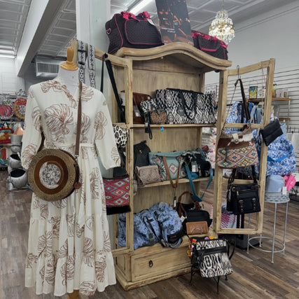 James Trading Co - The AnnexMannequin in a floral dress with a round bag stands next to a wooden shelf displaying patterned purses and bags. The store has a cozy, boutique feel.