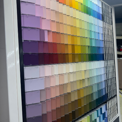 Display of neatly arranged paint swatches in a gradient from warm to cool colors, including pinks, reds, yellows, greens, and blues, in a store.