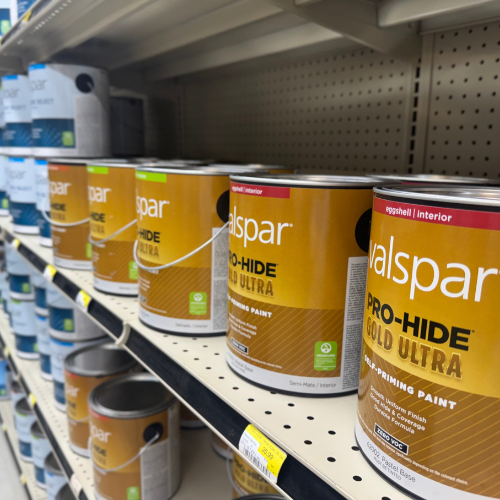 Shelf stocked with Valspar Pro-Hide Gold Ultra interior paint cans, featuring a gold and red label. Bright store lighting and organized display.