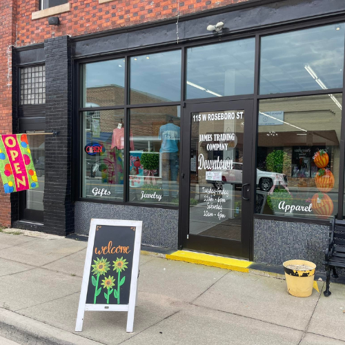 Storefront of a brick building with large windows displaying clothing and decor. A 